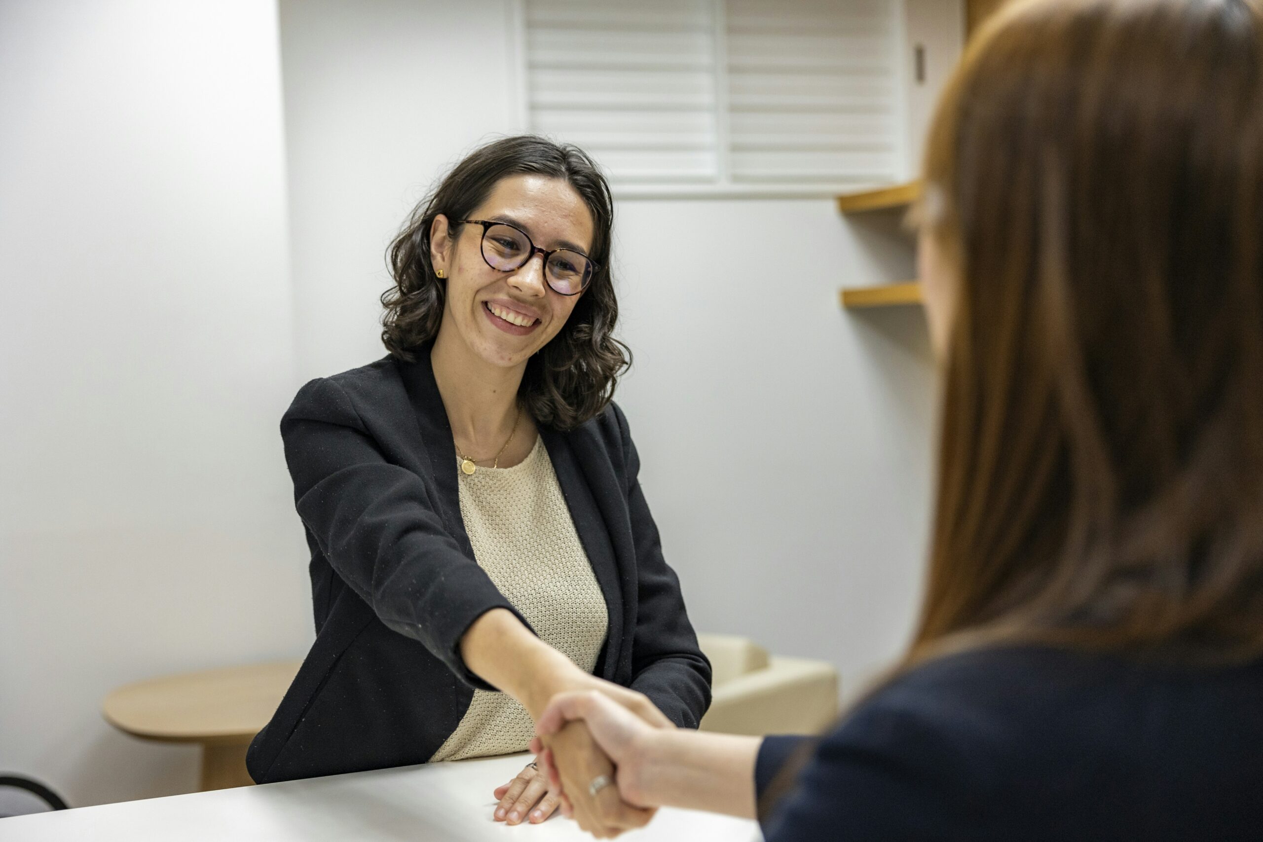 Two business people shaking hands at a desk.